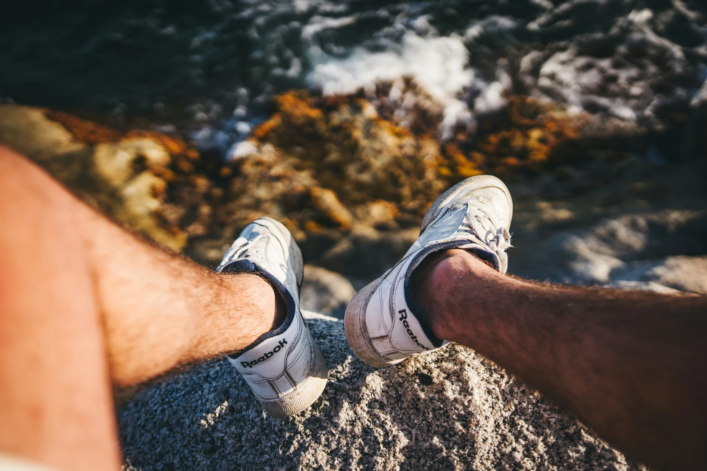 the legs of two people who are sitting on rocks by the ocean