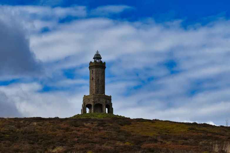 a tall, slender tower sits on top of a grassy hill