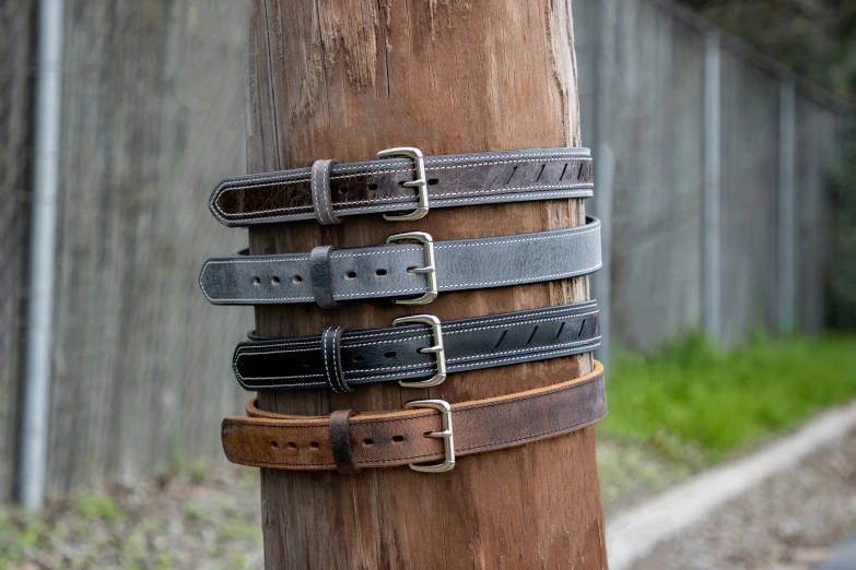 several leather belts lined up on a wooden post