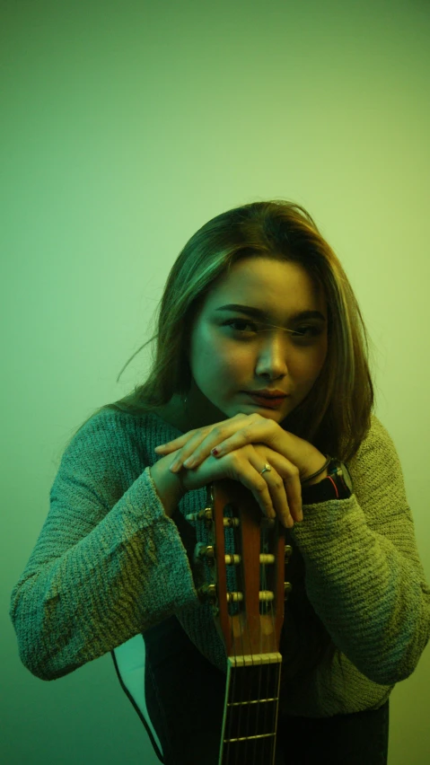 girl holding guitar near her face in green light