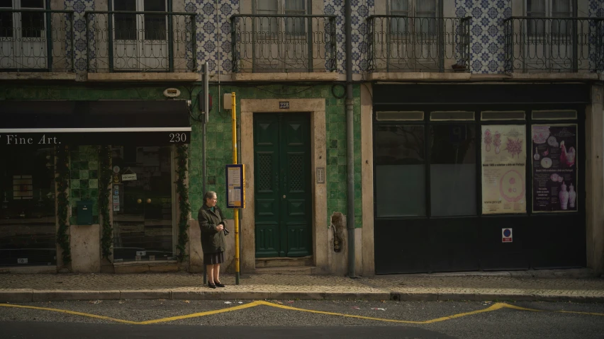 a woman is standing on the sidewalk next to a building with a tall green door