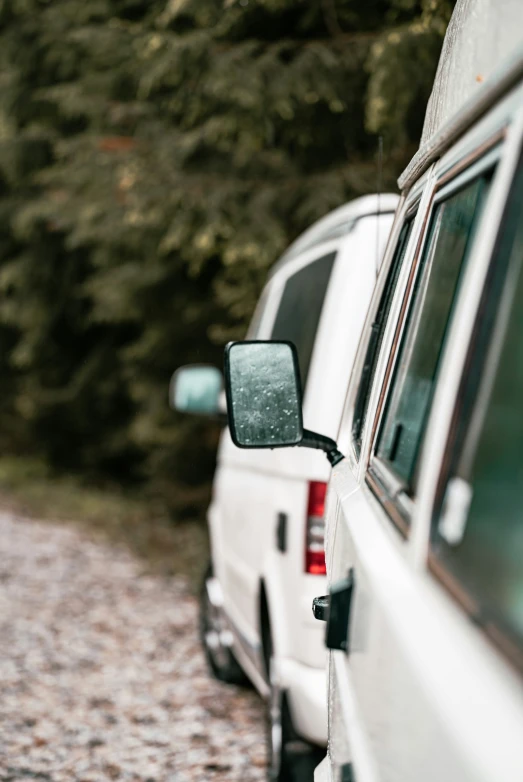 two white vans sit next to each other on a gravel road