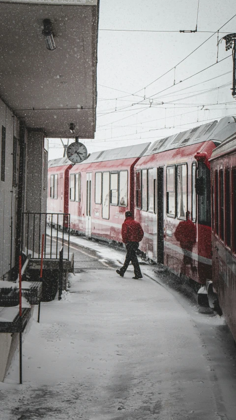 a man walks on snow covered pavement next to a train