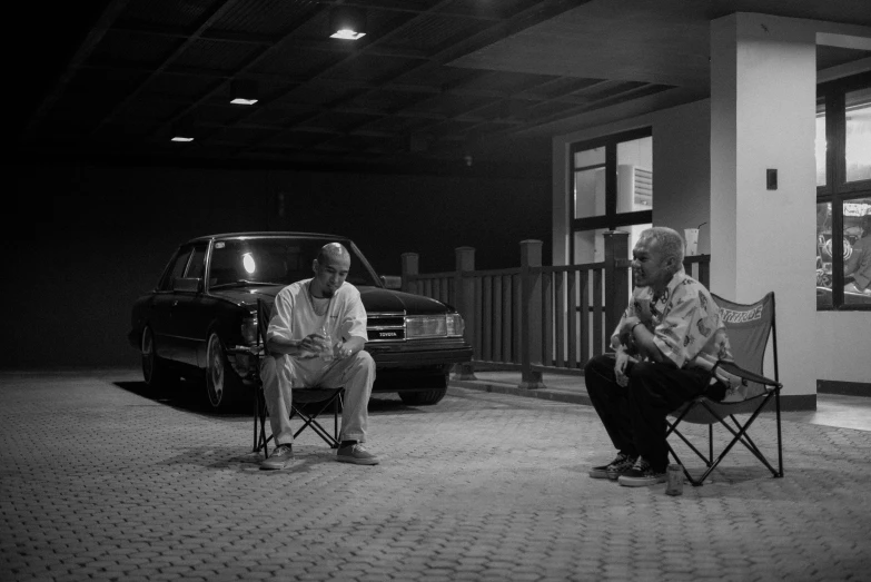 two men sit in their chairs next to their parked cars