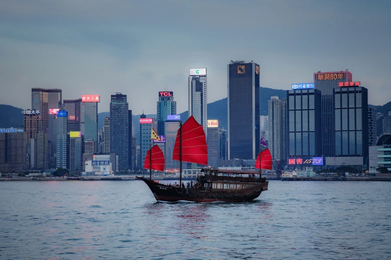 a sailboat is sailing along the river in front of skyscrs