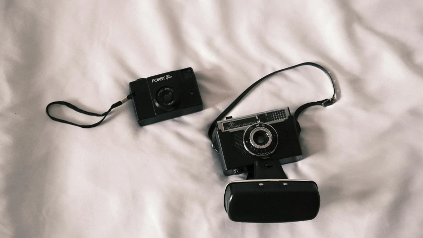 two small digital cameras sitting on top of a bed