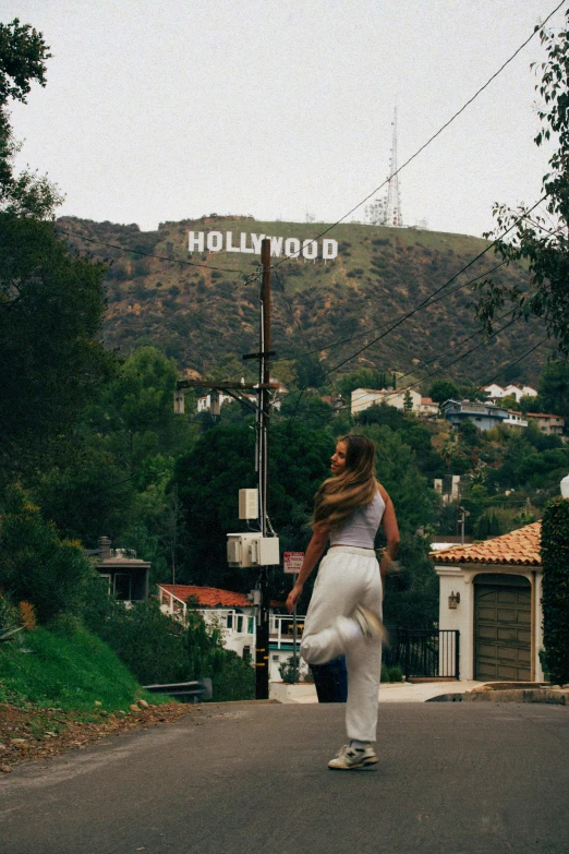 woman in white shirt on skateboard next to hollywood sign