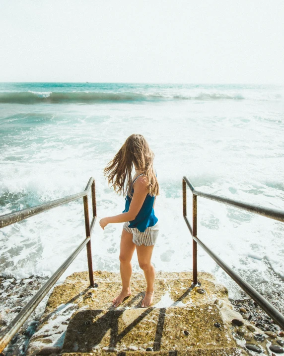 a little girl is walking up a railing near the beach