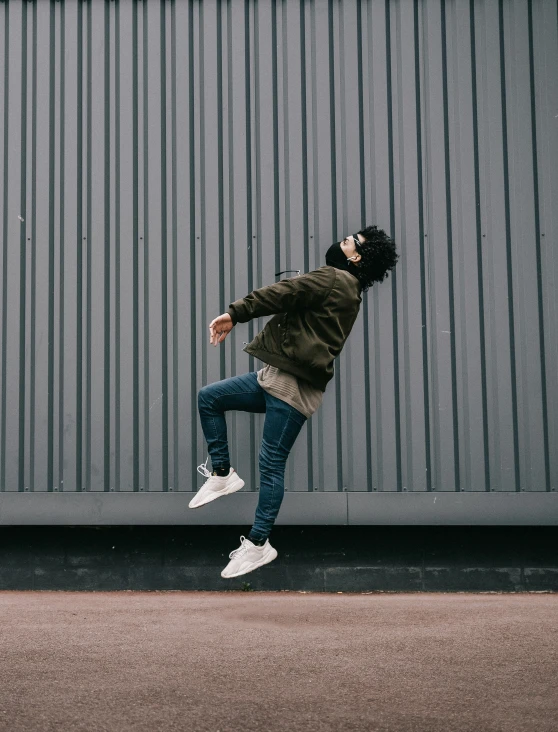 a man in jeans, a hoodie and white sneakers is doing a trick