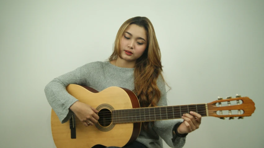 a girl wearing a gray sweater holding a brown guitar