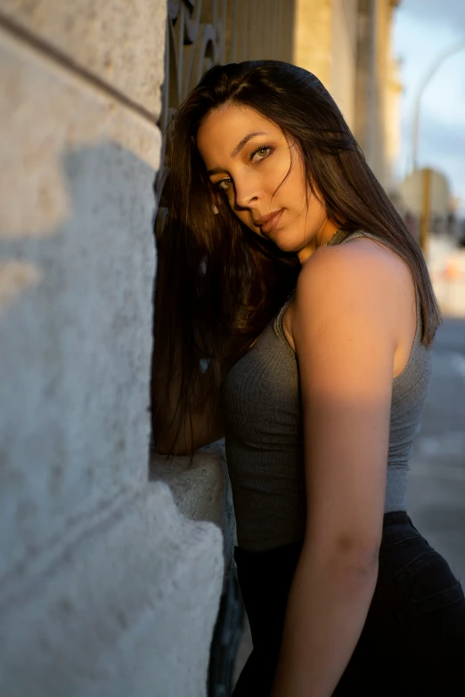 a beautiful young woman leans against a building