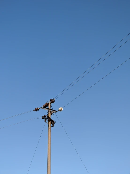 a street lamp and power lines in front of a blue sky