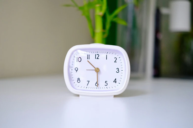 a square clock with three hands sits on a table