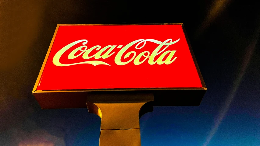 an illuminated sign for a coke cola company at night