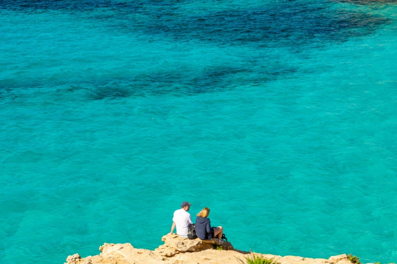 two people sitting on a rocky outcrop overlooking the water