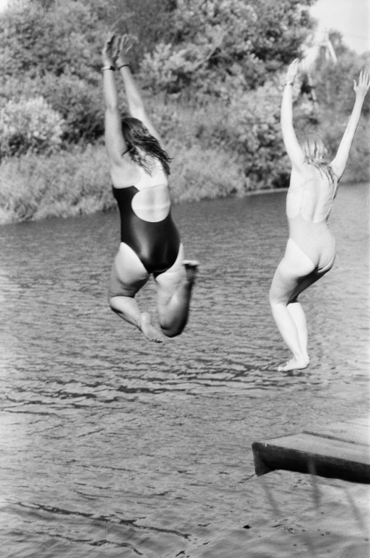 two young men jumping off a wooden dock into water