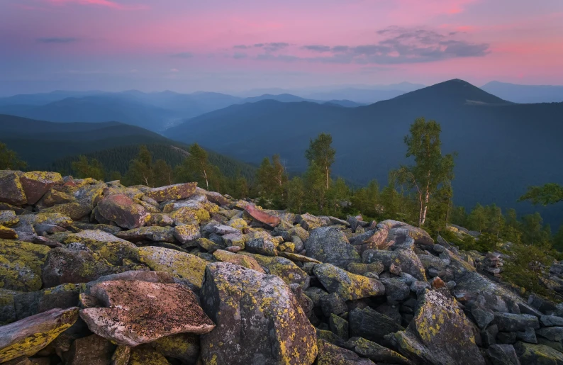 the sun is rising over the mountain tops, with rocks covered in moss