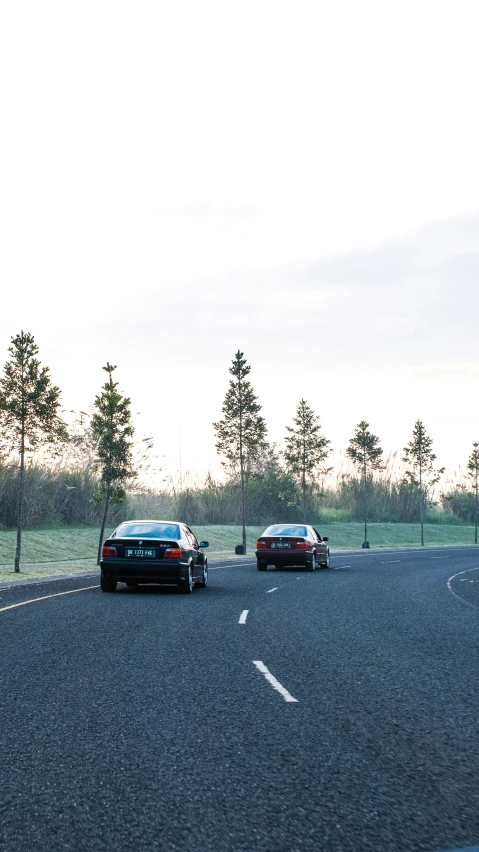 two cars are driving down a street beside a fence