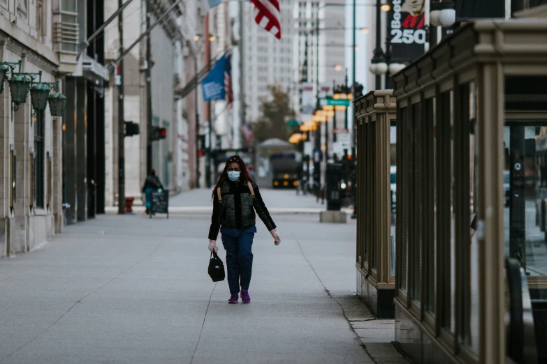 person walking down sidewalk wearing face mask next to buildings