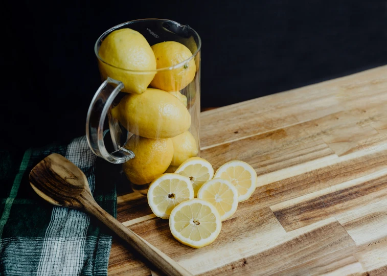 some lemons in a pitcher and some sliced on a table