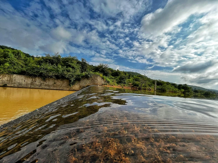 a body of water next to a hill under a cloudy sky