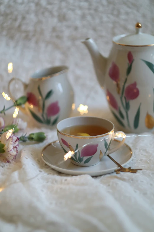a teapot, cup, and saucer with pink flowers on a white linen