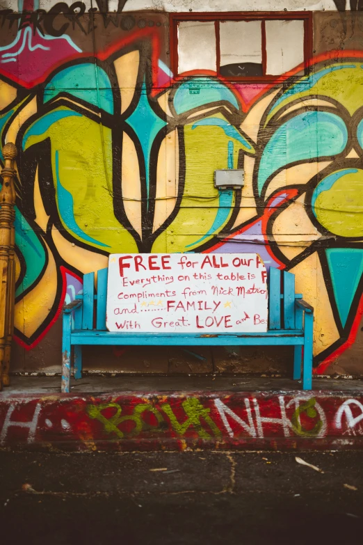 a blue bench sitting in front of a grafitti wall