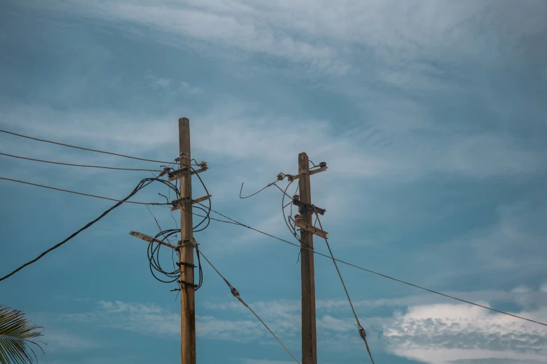 two power poles are close to each other and are standing in front of blue skies