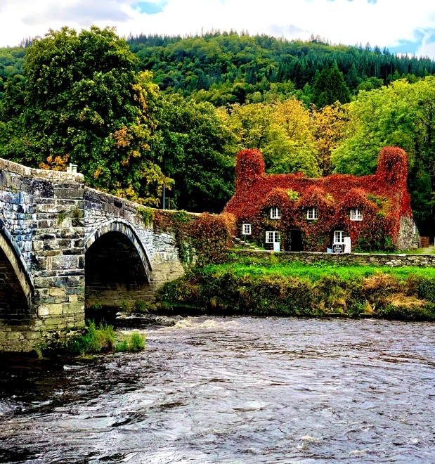 a bridge over a stream and a small red stone house on the hill