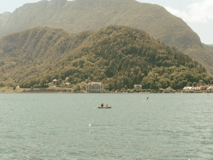 two people rowing a boat on a river near mountains