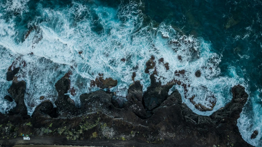 an aerial view shows ocean waves and rocks