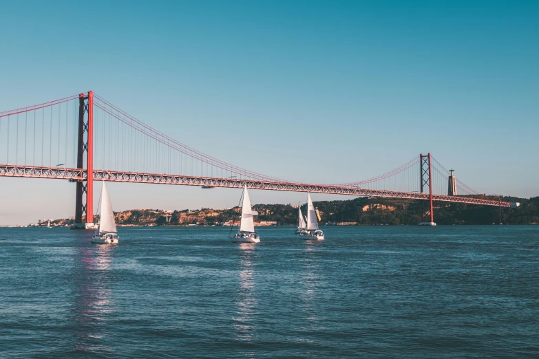 four sailboats in the water beneath a bridge