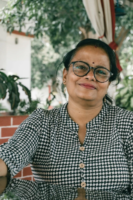 a smiling woman wearing eyeglasses with green trees in the background