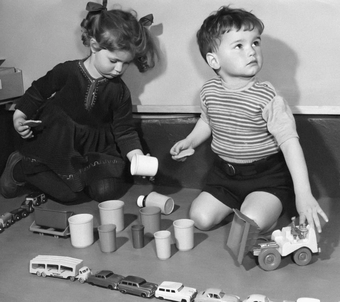 two young children sitting on the floor next to many toy cars