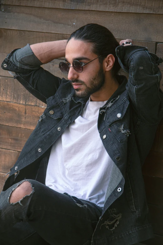 a man with his hair up in a ponytail is posing in ripped jeans and a jacket