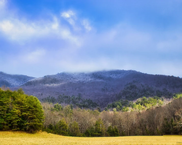 a mountain side field under clouds in the background