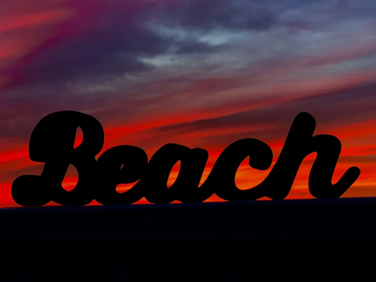 the word beach against a background of colorful clouds