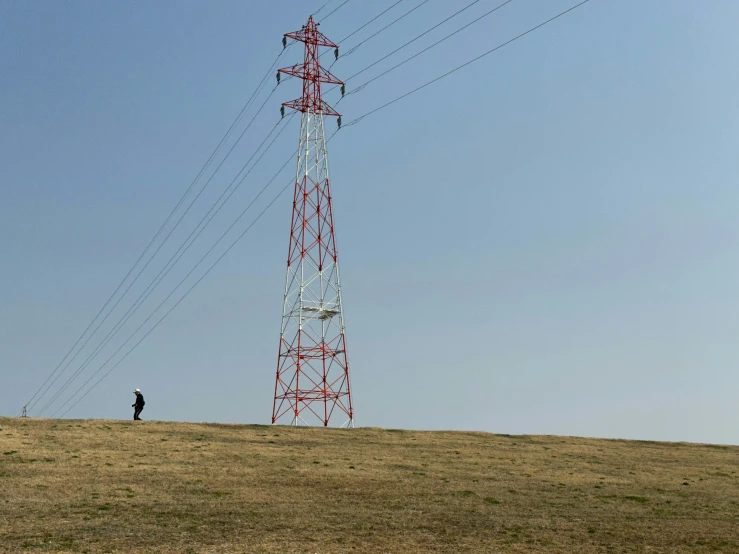 a man stands at the bottom of a hill in front of power lines