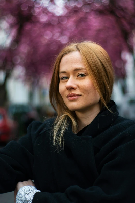 a woman stands near a tree with pink flowers