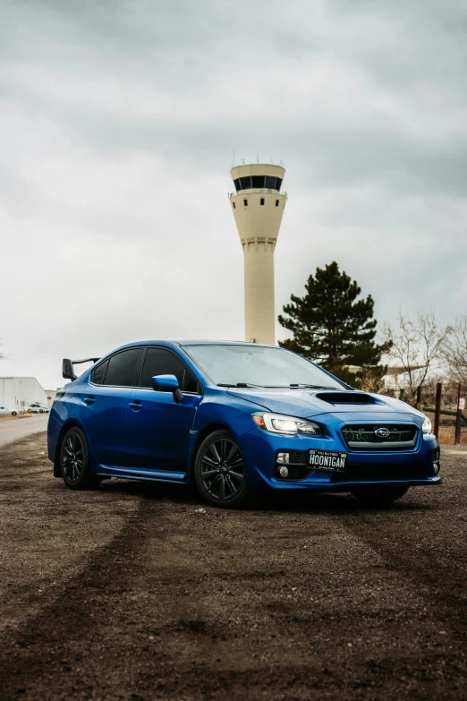 the subaru is blue while standing in front of a tall tower