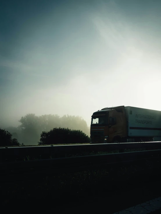 an orange truck driving down the street in front of the sun