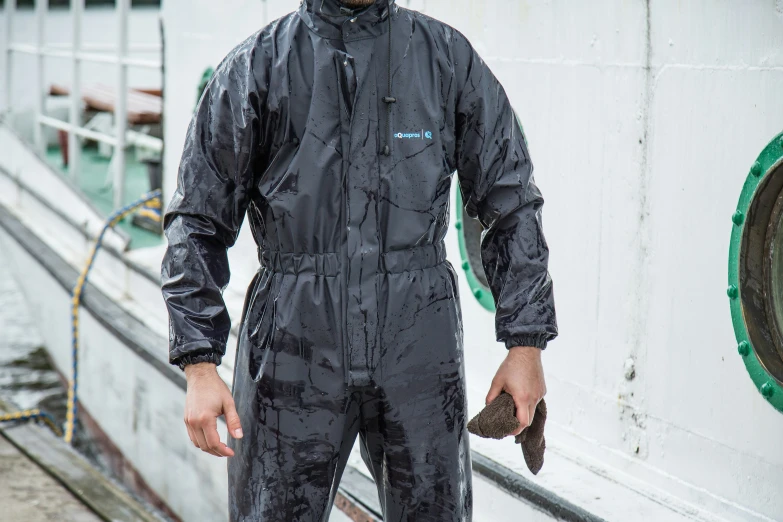 a man in black workwear and rubber boots stands next to a boat