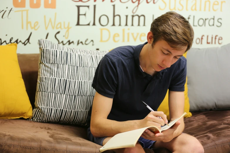 a young man on a couch holding a pen and a notebook