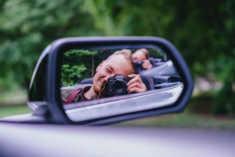 a person takes a selfie in the side view mirror of a car