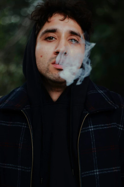 a man with a hoodie blowing smoke while wearing a black jacket