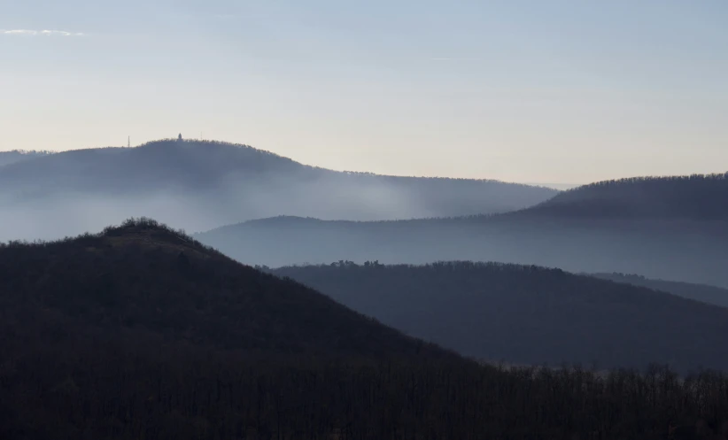 the view of several mountains and trees in a hazy sky