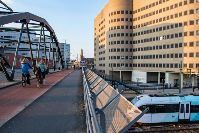 people on bicycles ride past an elevated train platform