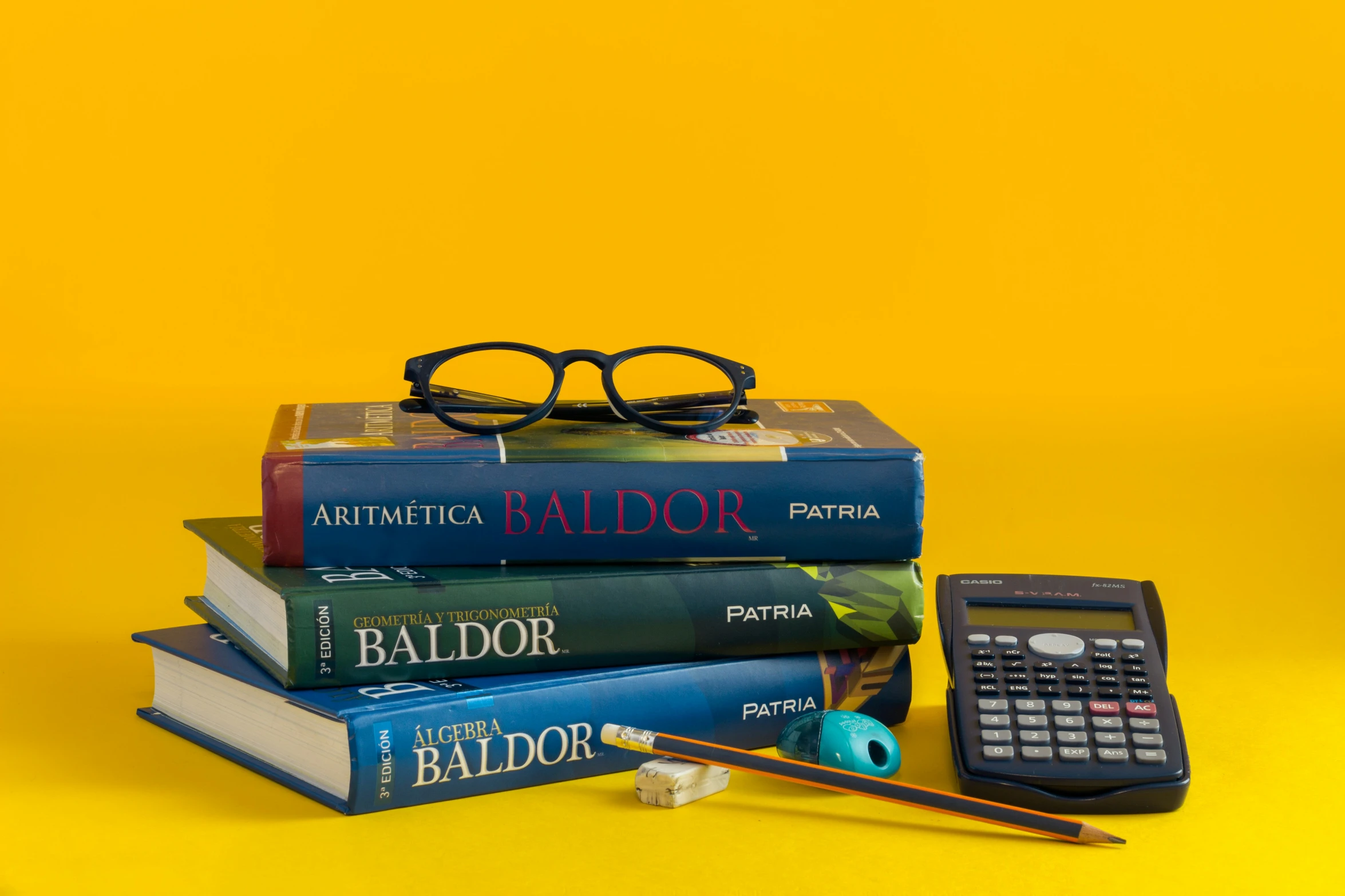 several books on a yellow table with eye glasses and pencil