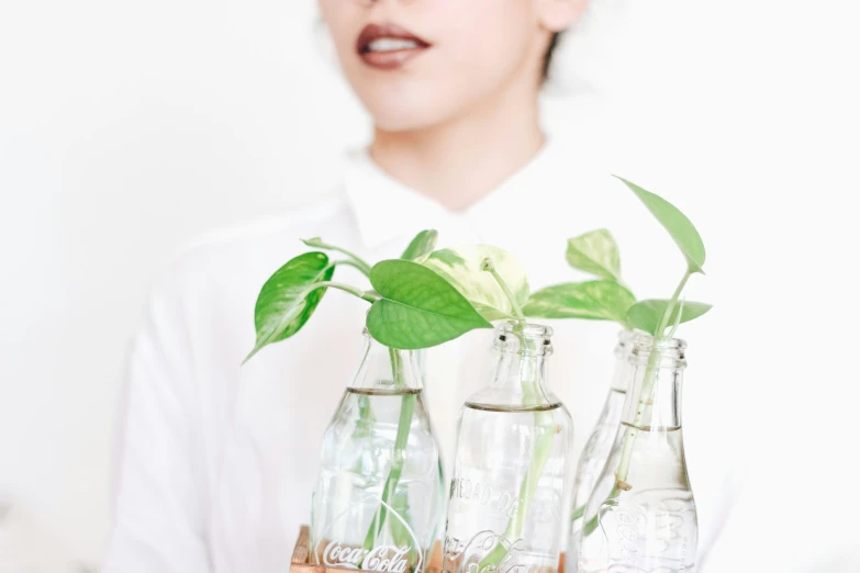 three small plants in glass vases next to a woman with pink lips