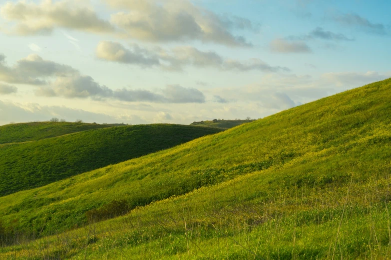 a green hill with hills on it and clouds in the sky